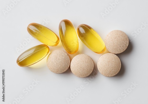 Three oval yellow capsules and three round beige tablets scattered on a white surface