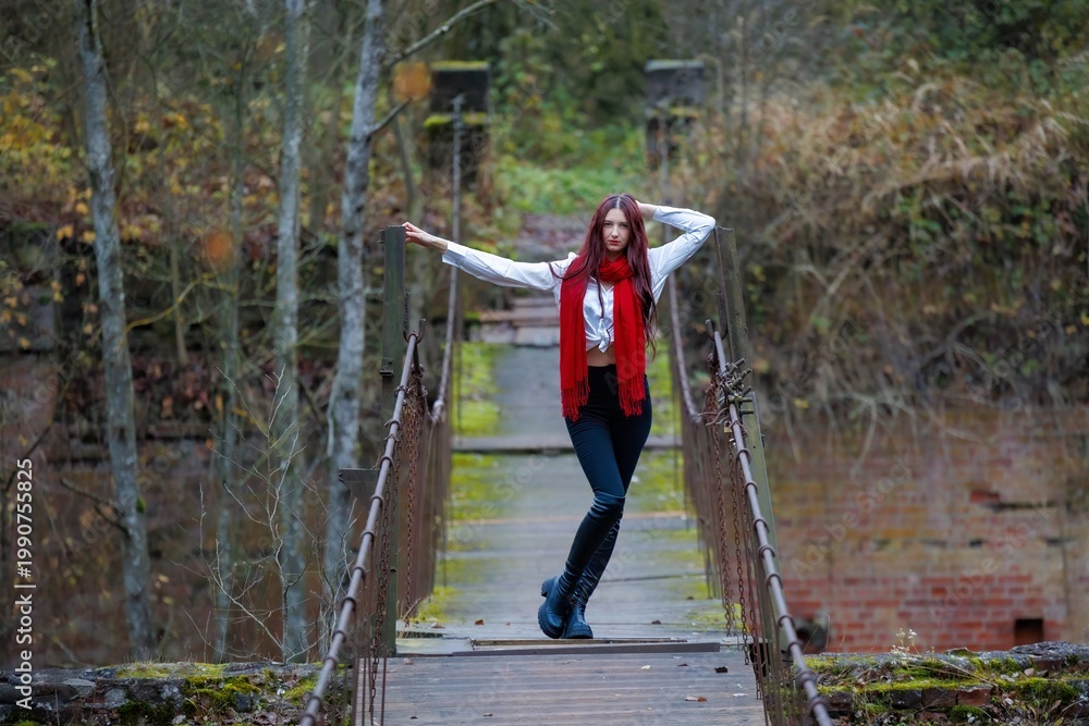 Naklejka premium Young Woman in Red Scarf Posing on Old Wooden Bridge in Autumn