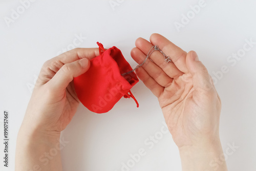 A Caucasian woman holds a red cloth bag. She takes out a silver chain from the bag.