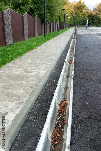 Urban concrete drain on an asphalt road along the sidewalk.