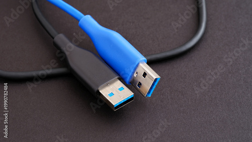 Two USB 3.0 Type-A cables in black and blue colors lying on a dark textured surface. Close up.