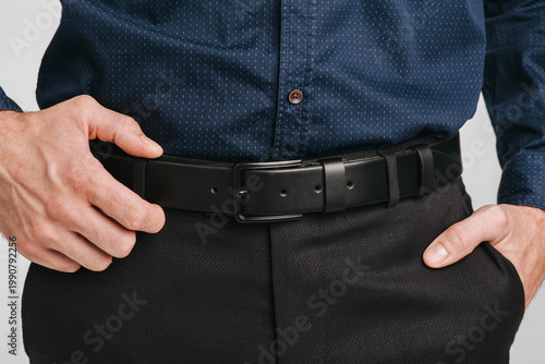 Bild auf Leinwand Close-up of a man wearing a black leather belt with a black buckle on dark trousers and a blue patterned shirt