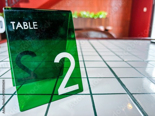 Green Acrylic Restaurant Table Number 2 on White Tiled Counter Top