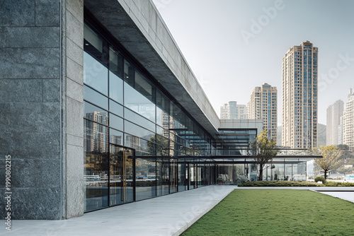 Modern Glass and Concrete Building Exterior with City Skyline and Green Lawn.