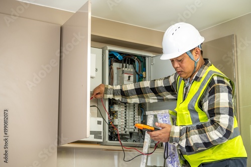 Construction worker in safety helmet and reflective vest inspecting electrical panel inside a modern residential building Electrician checking wi and circuit breaker system