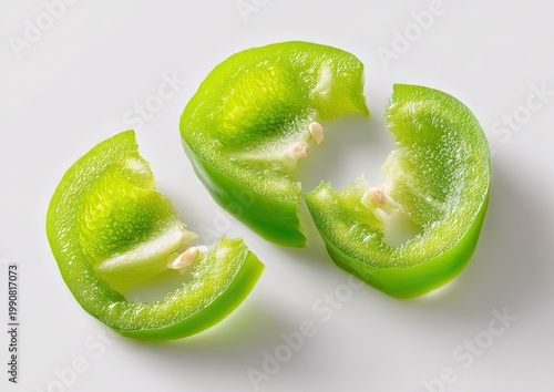 Sliced green pepper rings, showing seeds and white inner flesh on white