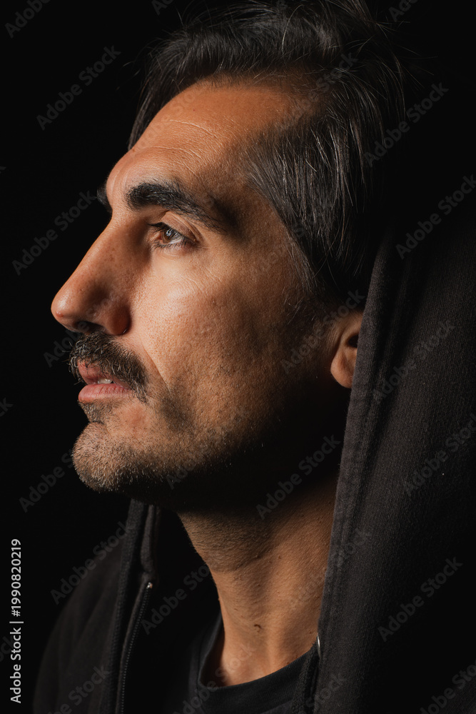 Fototapeta premium Man in dark hoodie gazes thoughtfully into the distance