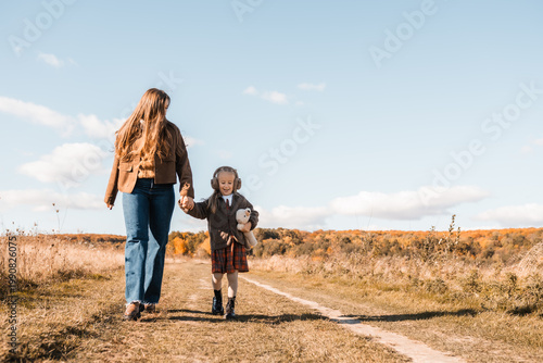 Mother and small child walking together along the autumn forest edge, exploring nature.
