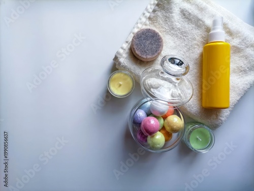Soft bath bombs rest beside candles and soap. Yellow spray bottle adds a bright, spa-like touch. Towel lies gently beneath glass jar and round sponge. Candles glow softly, inviting calm and relaxation