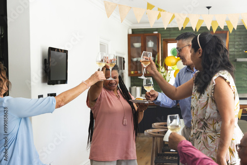 Multi-generational family and friends toasting in home kitchen, holding wine glasses and appetizers