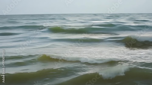Gentle ocean waves roll onto the shore, creating a rhythmic flow of water that reflects the soft light of the sky in a serene coastal landscape