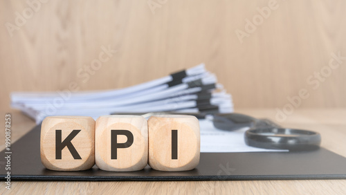 KPI acronym on wooden blocks. Blurred document stack and magnifying glass. Business performance concept.