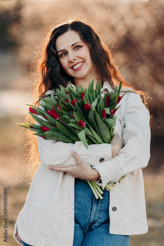 Beautiful woman smiling with long brown hair hold tulips bouquet in hand. Close up woman portrait outdoor.