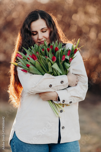 Beautiful woman smiling with long brown hair hold tulips bouquet in hand. Close up woman portrait outdoor.