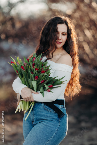 Beautiful woman smiling with long brown hair hold tulips bouquet in hand. Close up woman portrait outdoor.