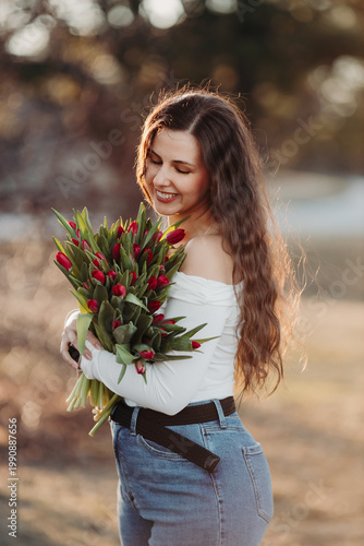 Beautiful woman smiling with long brown hair hold tulips bouquet in hand. Close up woman portrait outdoor.