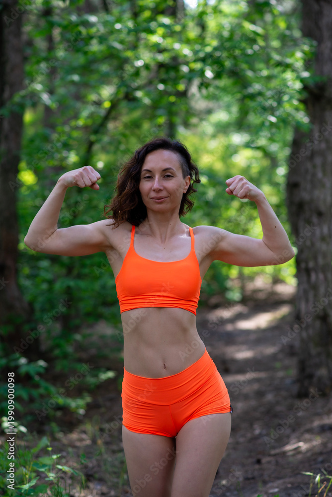 Fototapeta premium Woman flexing muscles in orange activewear outdoors
