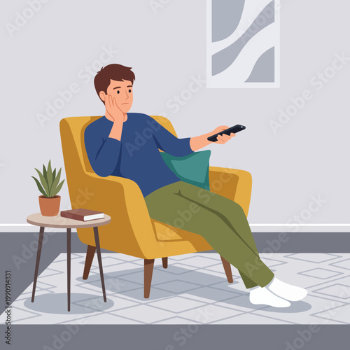 A young man is seated comfortably in a bright yellow chair, holding a remote control while watching television, conveying a sense of leisure and relaxation in a modern living room.