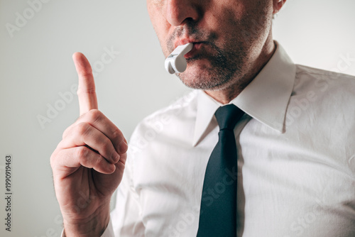Businessman blowing whistle with raised finger warning gesture, concept of whistleblower