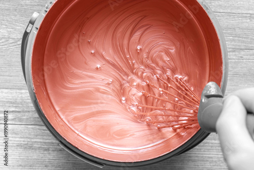 Person stirring mixing copper paint in a plastic paint tub container with a metal whisk. Decorating do it yourself home improvement concept.