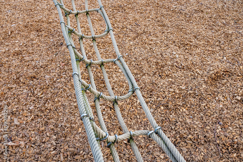 Close up of a sturdy rope climbing net with metal rings over a brown wood chip mulch in a playground