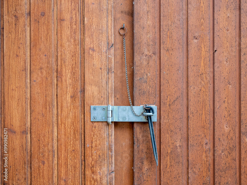 A close view of a brown wooden door features a metal latch, hinge and hanging chain