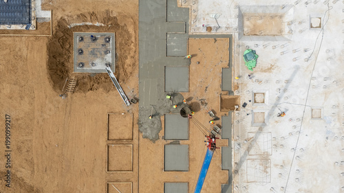 The process of laying the groundwork for a new building, seen from above, involves pouring concrete for the foundation. Workers on the construction site, seen from above, are using a construction