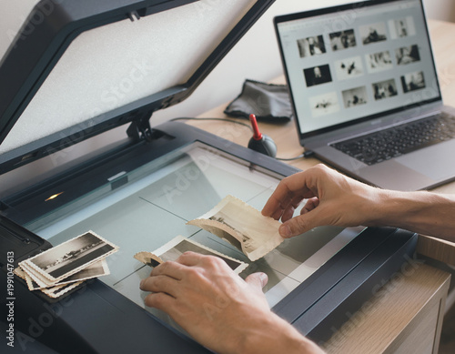 Hands carefully arrange old photos on a scanner bed. A person digitizes vintage paper prints, preserving history. Modern technology captures past images for a digital archive.