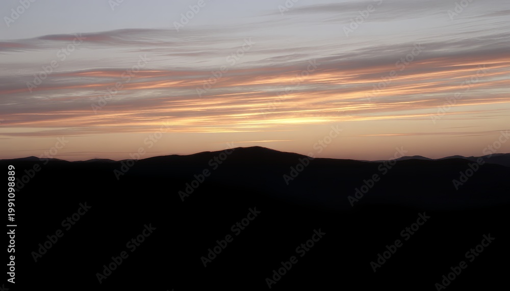 Obraz premium The sun sets behind a mountain range casting a warm orange glow on the clouds in the evening sky