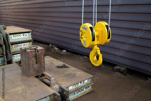 Vászonkép Yellow overhead crane hook suspended above heavy metal counterweights with marke