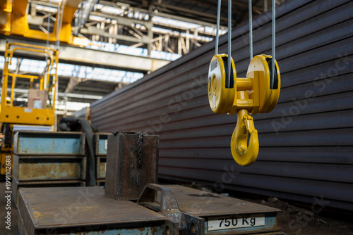 Принти на полотні Industrial crane hook and pulley system hanging near stacked metal beams and cou