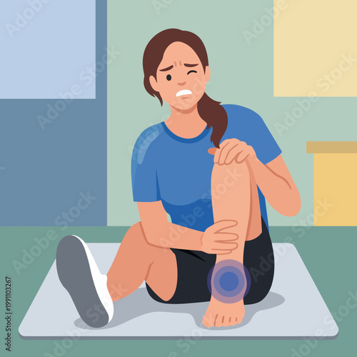 A young woman is sitting on a mat indoors, displaying discomfort while holding her injured ankle. This image portrays struggle, recovery, and determination to heal from injury.