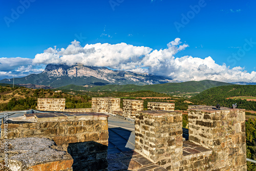 Ainsa Castle in the medieval village of Ainsa in Spain surrounded by stone walls with an elevated path leading to it.