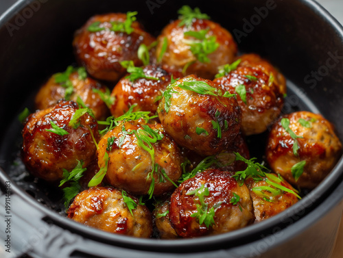 Glazed meatballs cooking in air fryer basket with herbs