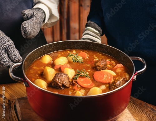 stewpot being carried to a table with hot mitts