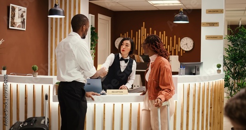 Friendly asian receptionist offering room key to happy guests after check in process is finalized. Busy exhausted hotel manager ensuring booking paperwork details are correct