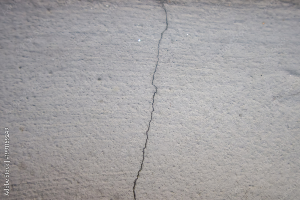 Fototapeta premium Cracked concrete wall close up. Grey cement surface with visible fracture line, structural damage concept, minimal industrial background, rough texture, high resolution.