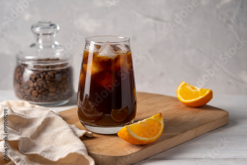 Coffee with orange juice bumble in a tall glass with ice on a light background with coffee beans, fruits and morning shadows