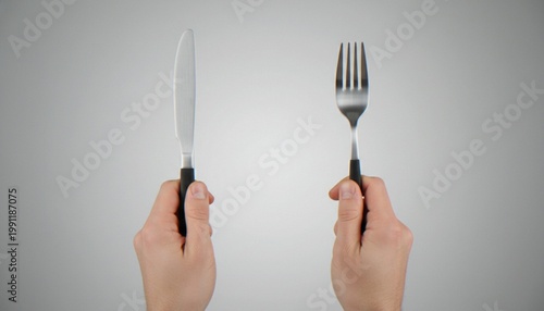 Tableau sur toile A close-up of a person's hands holding a stainless steel knife and fork vertically against a neutral gray background