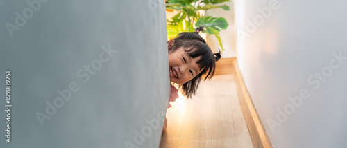 Bild auf Leinwand little asian children kid playing hide and seek standing behind the sofa, Adorable child having fun in the home