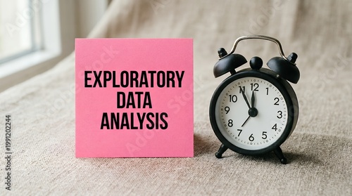 A pink sticky note with the words Exploratory Data Analysis sits beside a vintage black alarm clock on a textured neutral surface statistics business research information