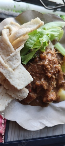 A delectable Indonesian salad served with crispy crackers on a disposable plate, showcasing fresh ingredients