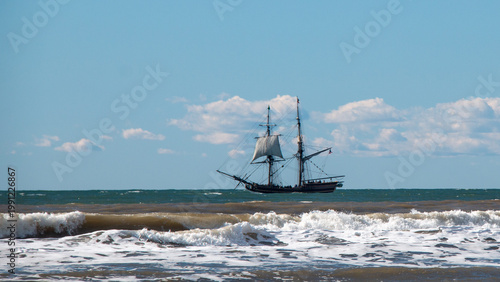 Wooden tall ship which is a full-scale 18th-century brig replica sailing through white-capped waves along the California coastline near Ventura, United States