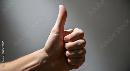 Close-up shot of a human hand making a thumbs-up gesture against a subtly lit grey background, conveying messages of approval, success, positivity, and excellent feedback