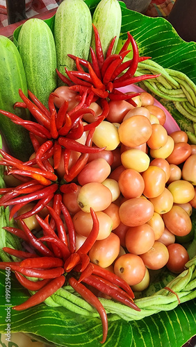 A close-up of colorful and vibrant Thai Som Tum (papaya salad) ingredients. Features fresh tomatoes, bunches of fiery red chilies, crisp cucumbers, and long beans in a market display.