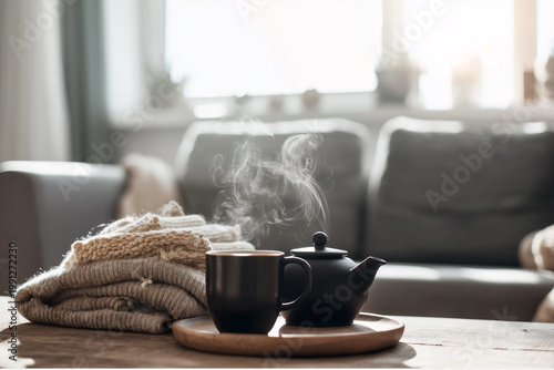 Steaming cup of tea and teapot on wooden tray with knitted sweater in cozy living room, hygge lifestyle and autumn comfort concept