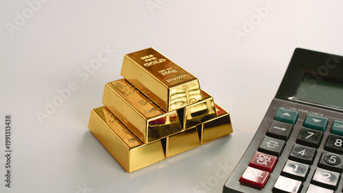 Close up of an office calculator next to a stack of gold bars for accounting and financial planning.