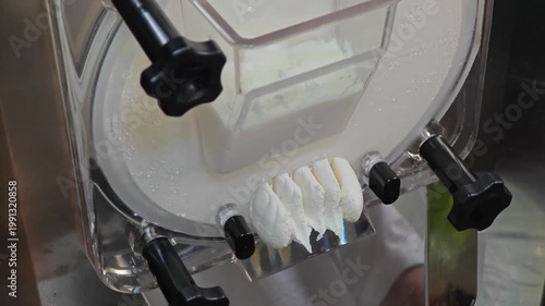 Gelato machine dispensing creamy gelato into a container. Ice cream making process.