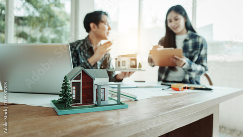 Photography Real estate agents review documents with house model and laptop on desk in bright office, home buying or property investment consultation
