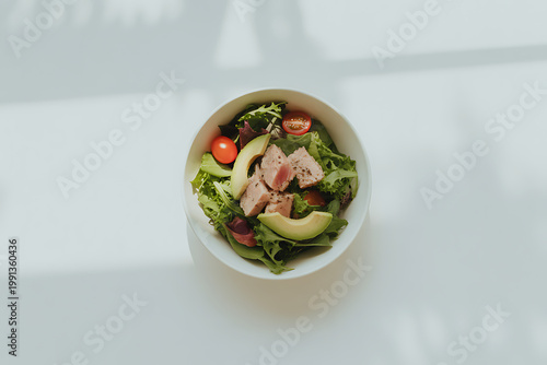 Tasty salad with tuna avocado and tomatoes in white bowl on table